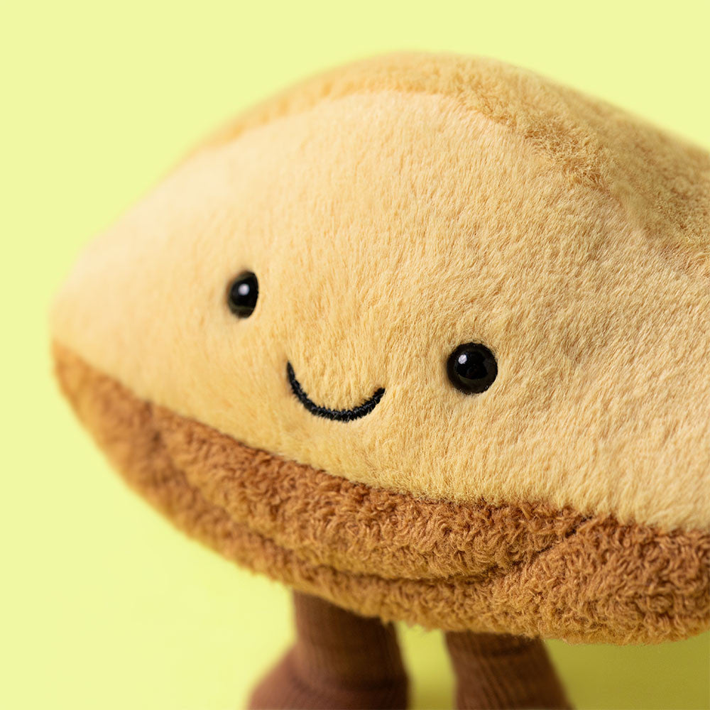 Close-up of the happy face of the Amuseables Margaux Madeleine plush toy by JellyCat, emphasizing its friendly eyes and fluffy feel.