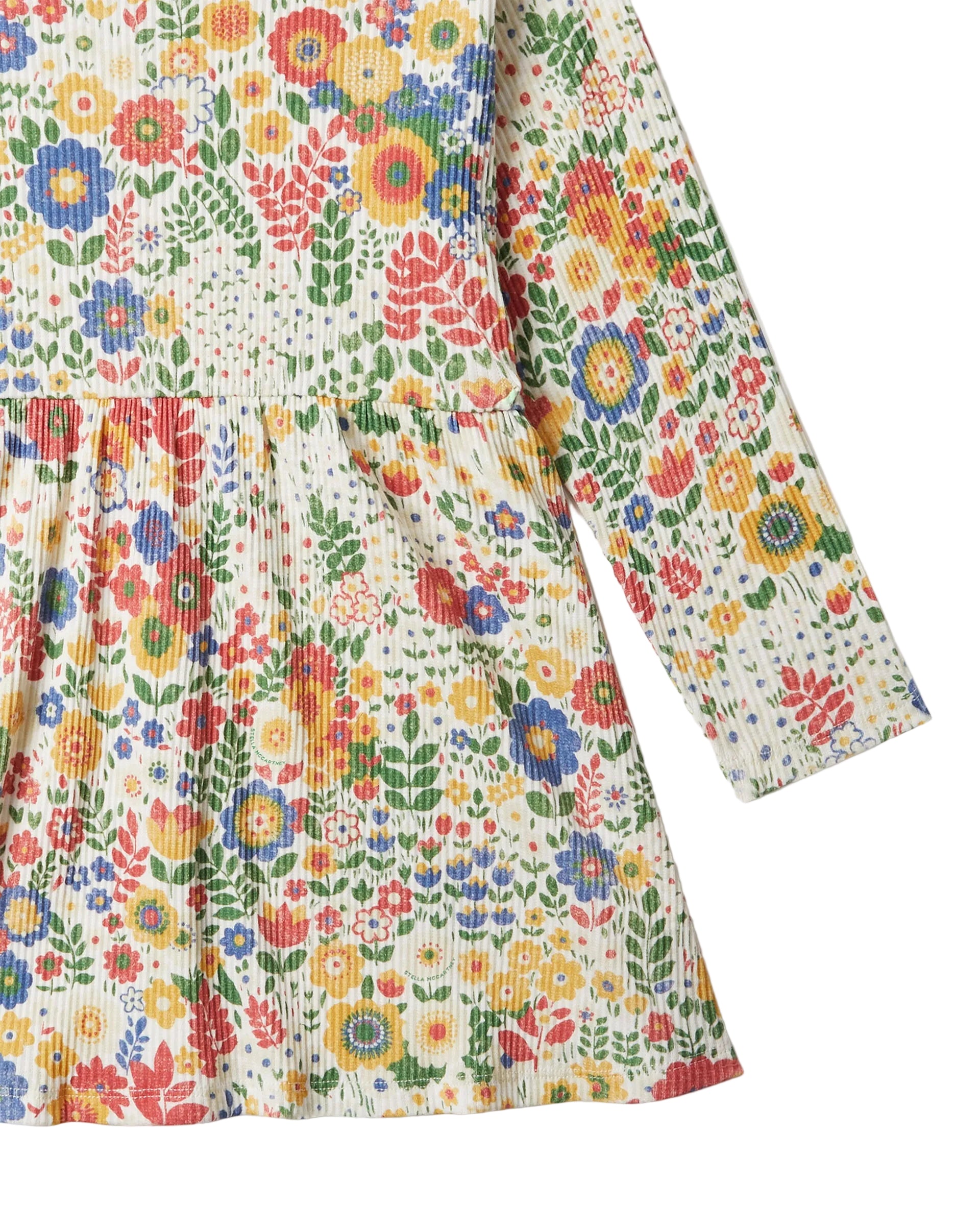 A close-up of a long-sleeve children's dress with a colorful floral print on a textured, ribbed cream fabric, set against a plain white background.
