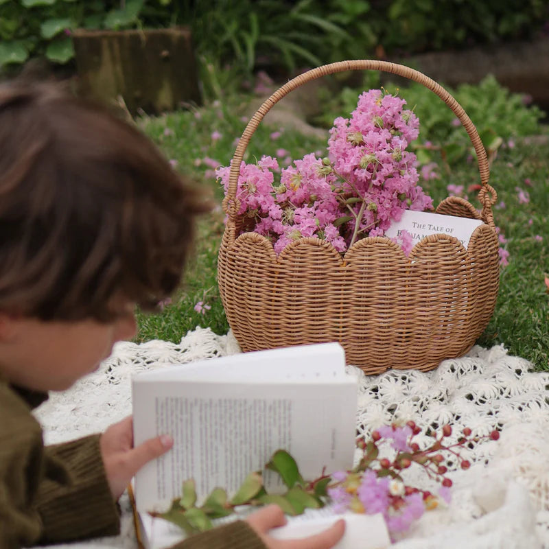 A child enjoying the outdoors with the Olli Ella Petal Basket - Natural filled with pink flowers, ideal for playdates and nature walks.