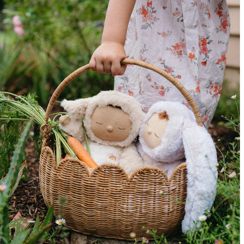 A little girl holding the Olli Ella Petal Basket - Natural, featuring plush dolls and a fresh carrot, highlighting its versatile use for imaginative play.