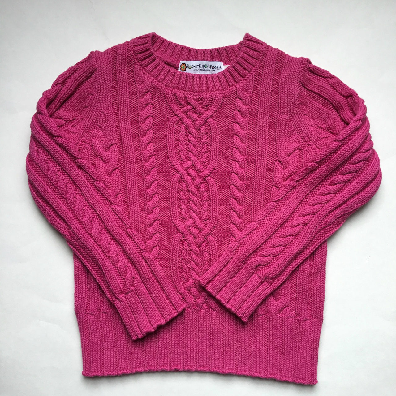 A vibrant pink cable knit sweater presented flat, emphasizing its soft texture and beautiful design. This stylish option is from Pocket Full of Posies, specializing in unique cable knit sweaters.