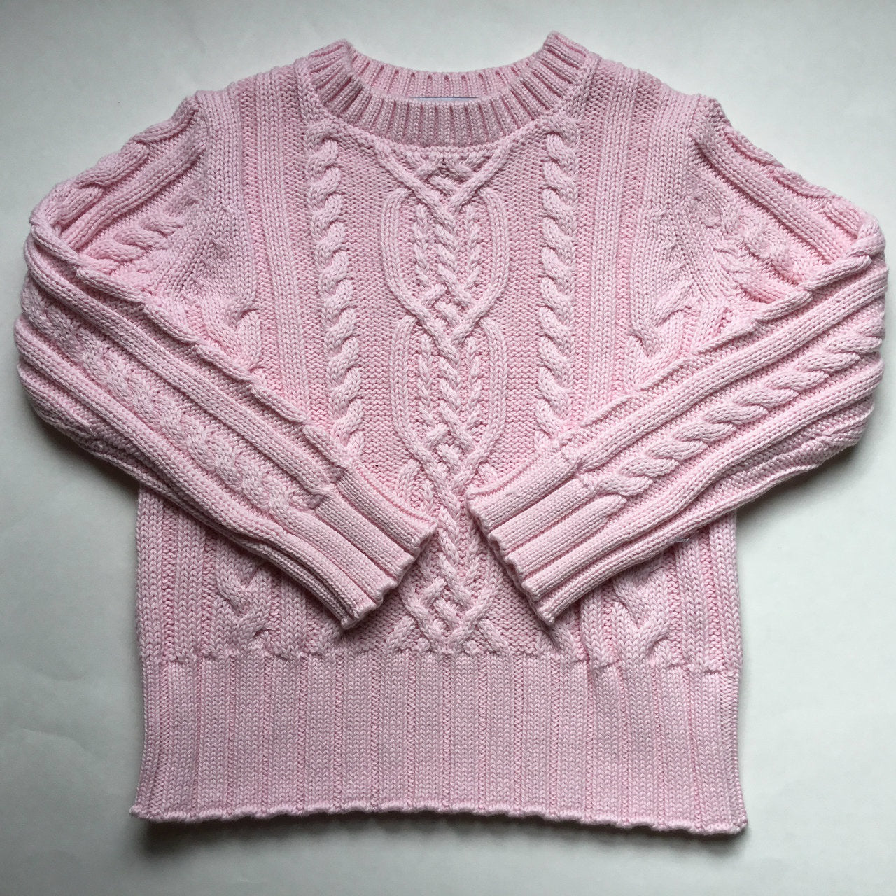 A pink cable knit sweater displayed flat, showcasing intricately woven patterns and cozy texture. This design is from Pocket Full of Posies, known for their stylish cable knit sweaters that offer comfort and fashion.