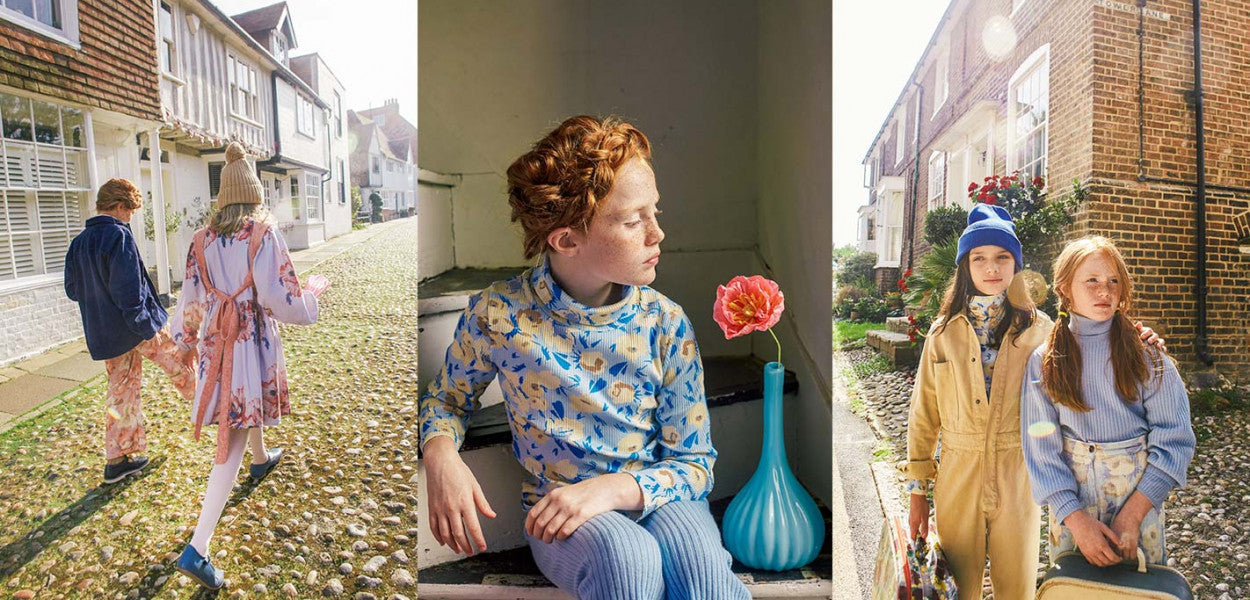 Stylish children wearing Morley clothing walking down a charming cobblestone street, showcasing bright colors and original prints in their outfits. The girl in a floral dress and the boy in a dark jacket embody the playful essence of Morley fashion.