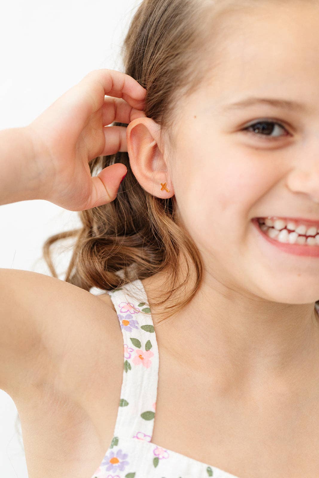 A cheerful girl adjusting her Cross Earrings by Pip Pop Post, highlighting their secure fit and playful style.