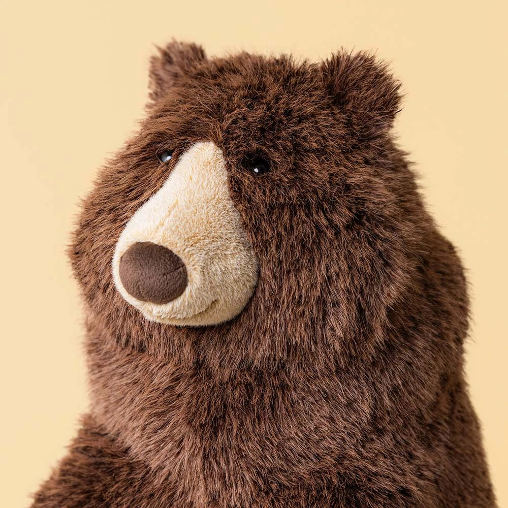 Bizzlestomp Bear JellyCat stuffed animal shown from the side with a cuddly sitting design