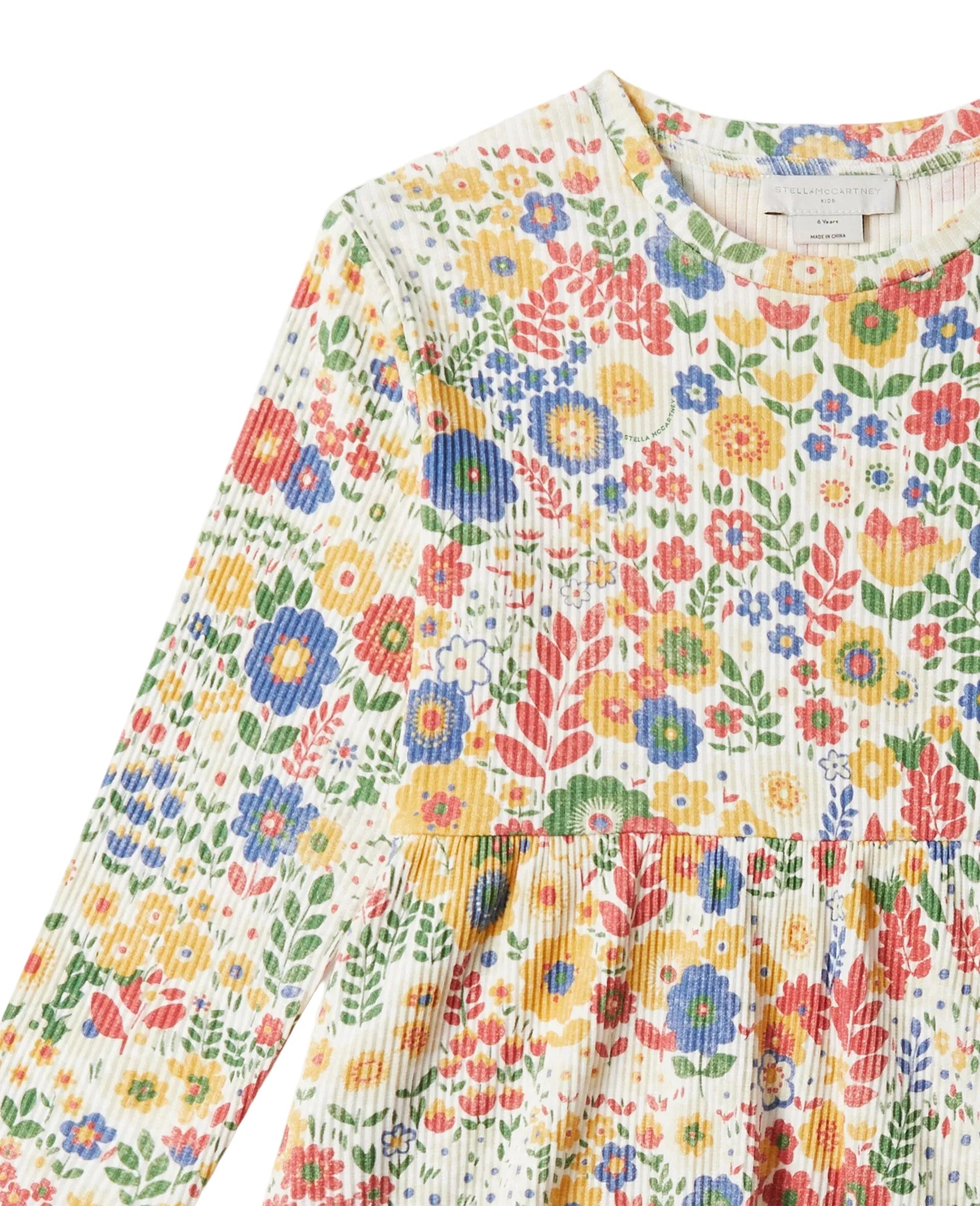 A close-up of a long-sleeve top with a colorful floral print on a textured cream ribbed fabric, featuring a round neckline and a gathered waist seam.