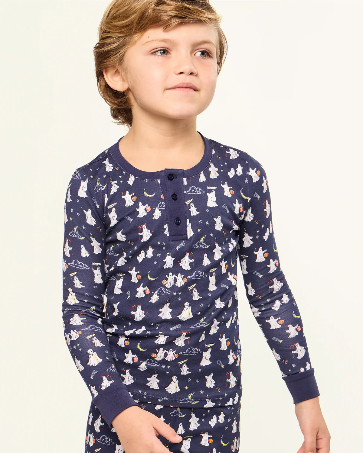 Front view of a child wearing the Kids Pima Snug Fit Pajama in Spooky Slumber by Petite Plume, featuring a happy expression and playful ghost patterns.