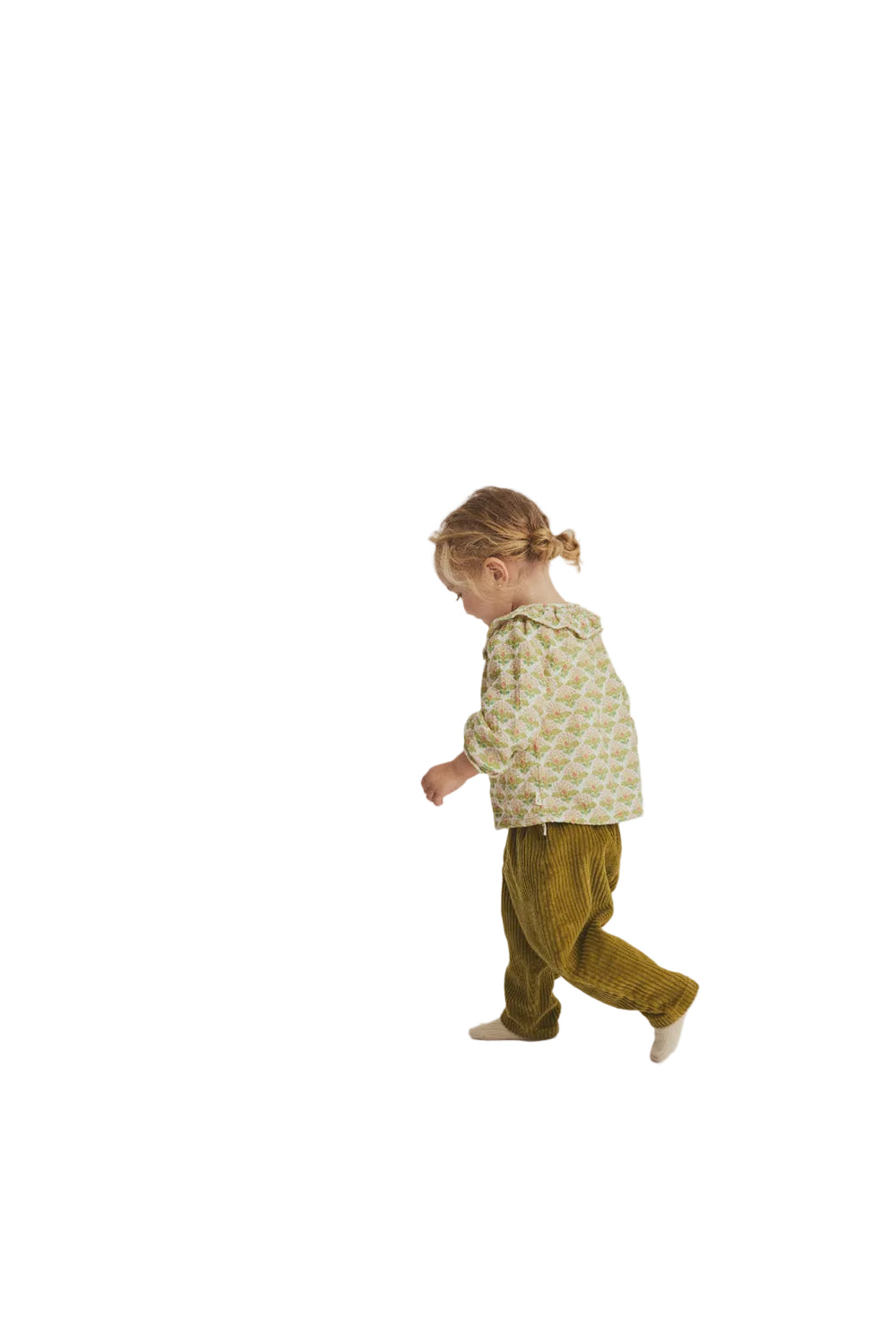 Child wearing a patterned shirt and green pants on a plain background
