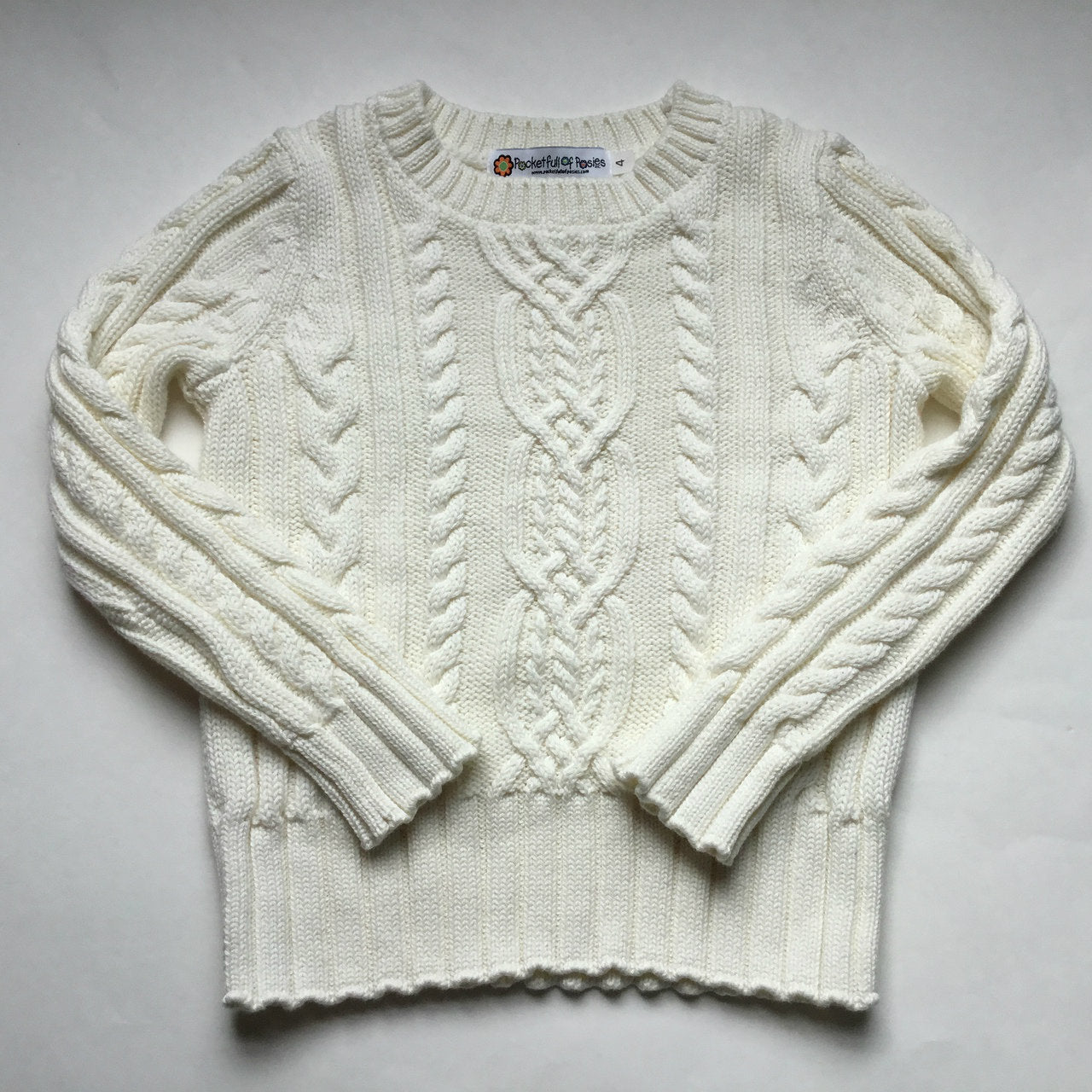 A classic white cable knit sweater laid out to highlight its detailed craftsmanship and cozy fit. This elegant piece is part of Pocket Full of Posies' collection of cable knit sweaters, perfect for everyday wear.